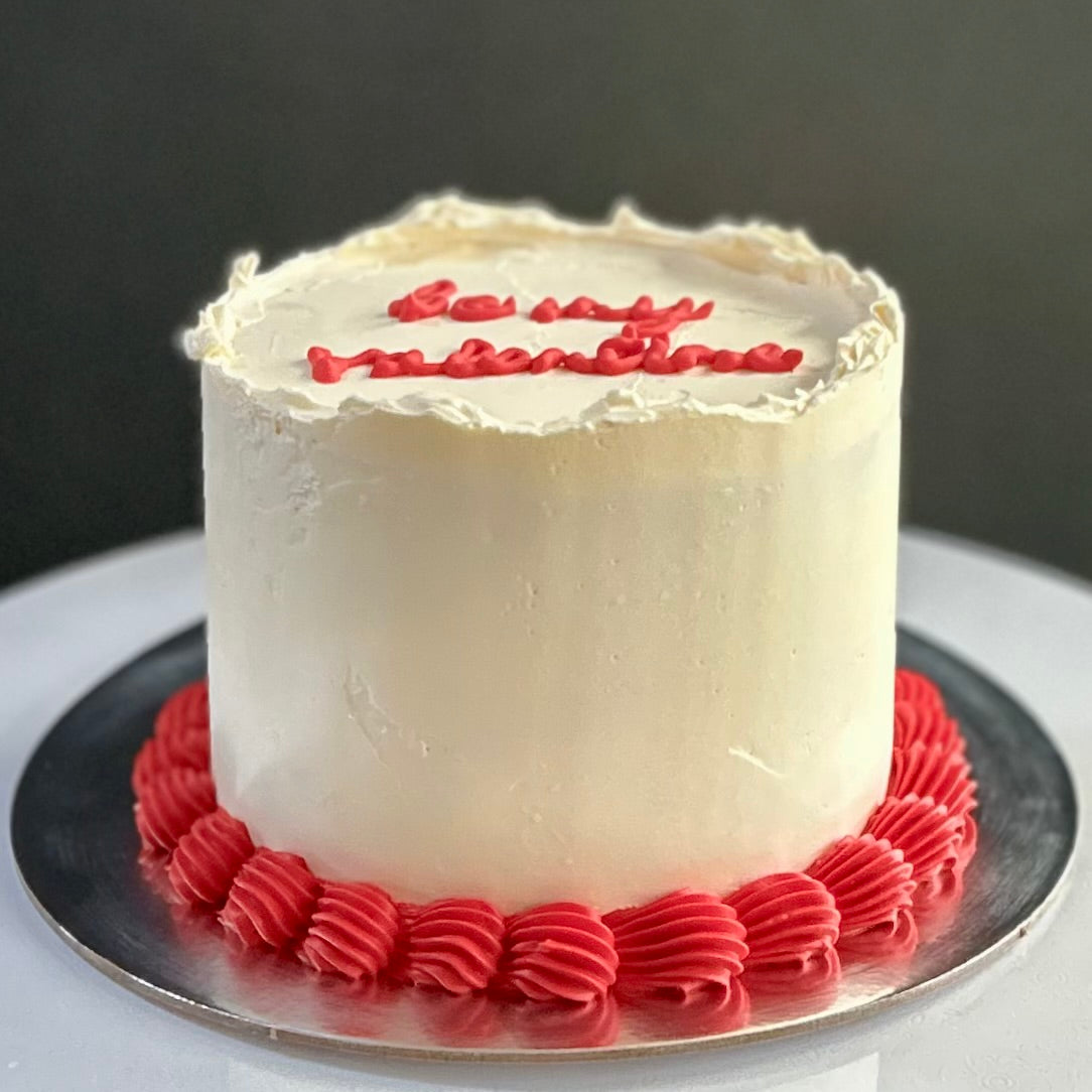 White cake with red text and decorations on a dark background
